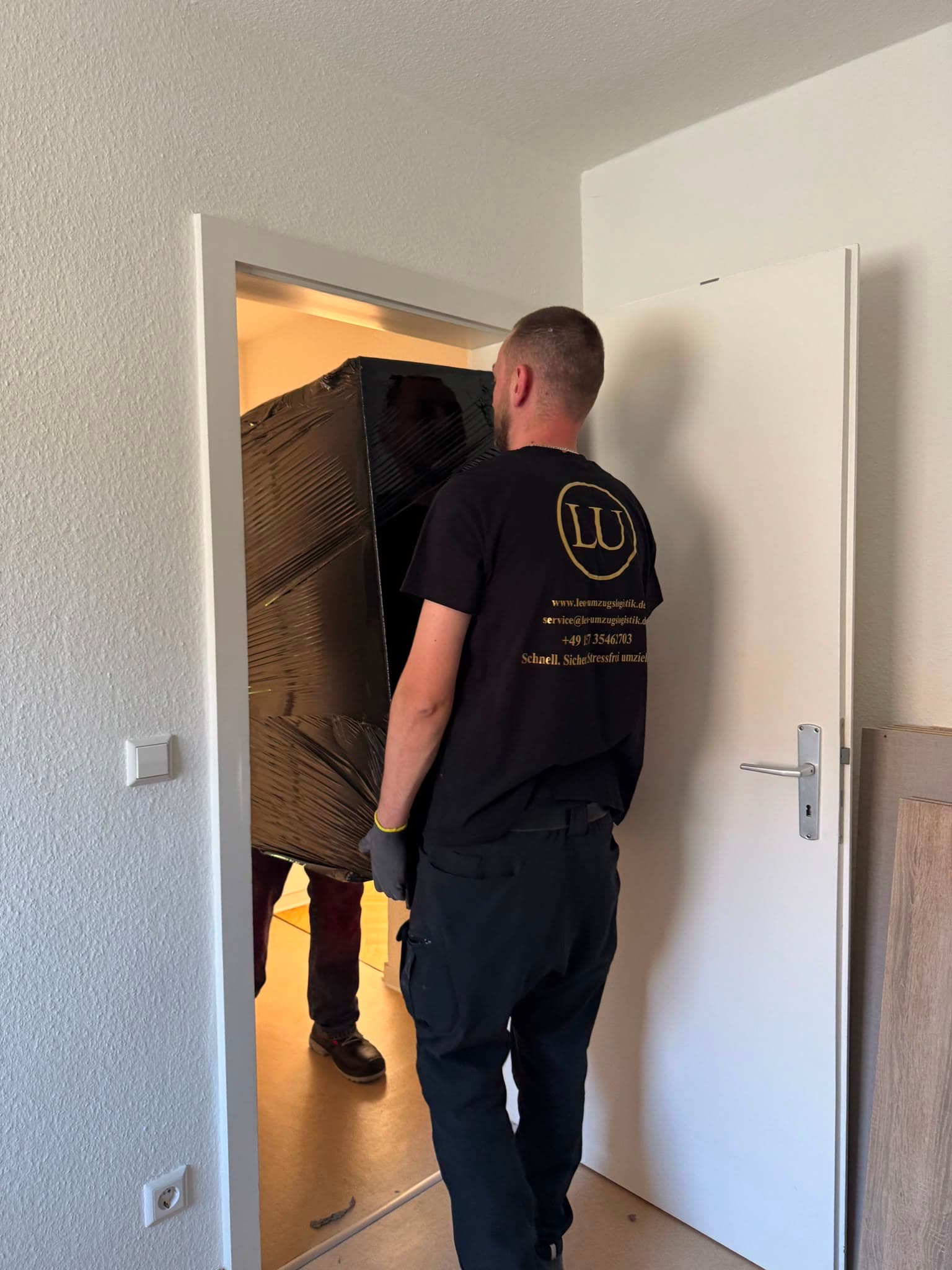 Zwei Mitarbeiter tragen einen verpackten Schrank durch einen engen Türrahmen