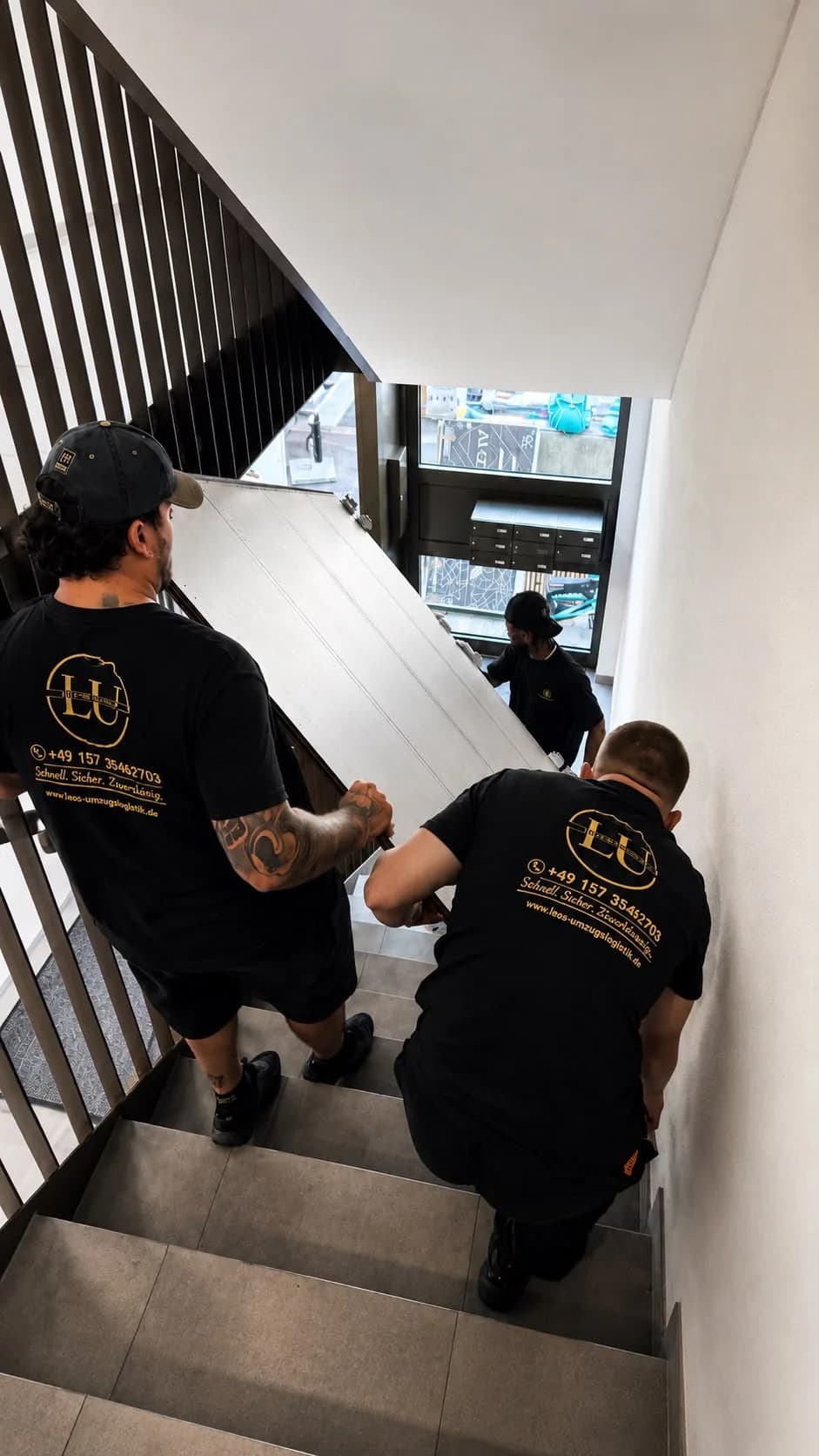 Zwei Mitarbeiter von Leos Umzugslogistik tragen ein großes Möbelteil durch ein Treppenhaus nach unten
